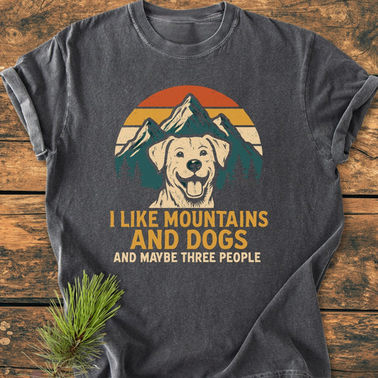 Charcoal-gray I Like Mountains And Dogs - Vintage Wash Tee featuring a happy dog graphic with a mountain sunset, bold slogan, and relaxed fit, laid on wood, highlighting its cozy, durable design.