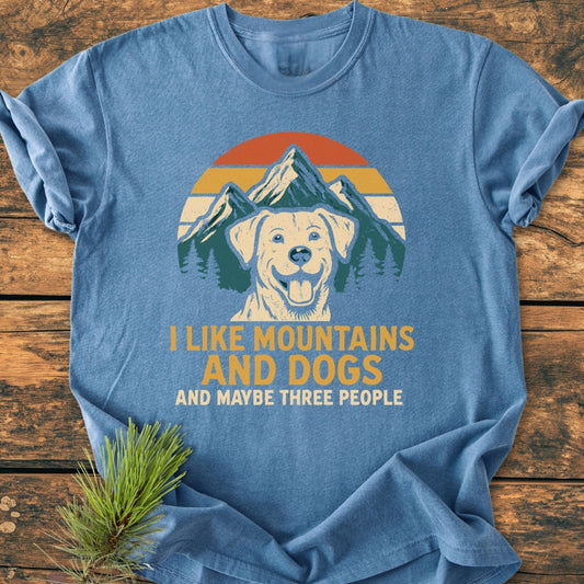 Heather-blue I Like Mountains And Dogs - Vintage Wash Tee features retro mountain and dog graphic with bold text, laid on wooden surface, showcasing its relaxed fit and durable stitching.