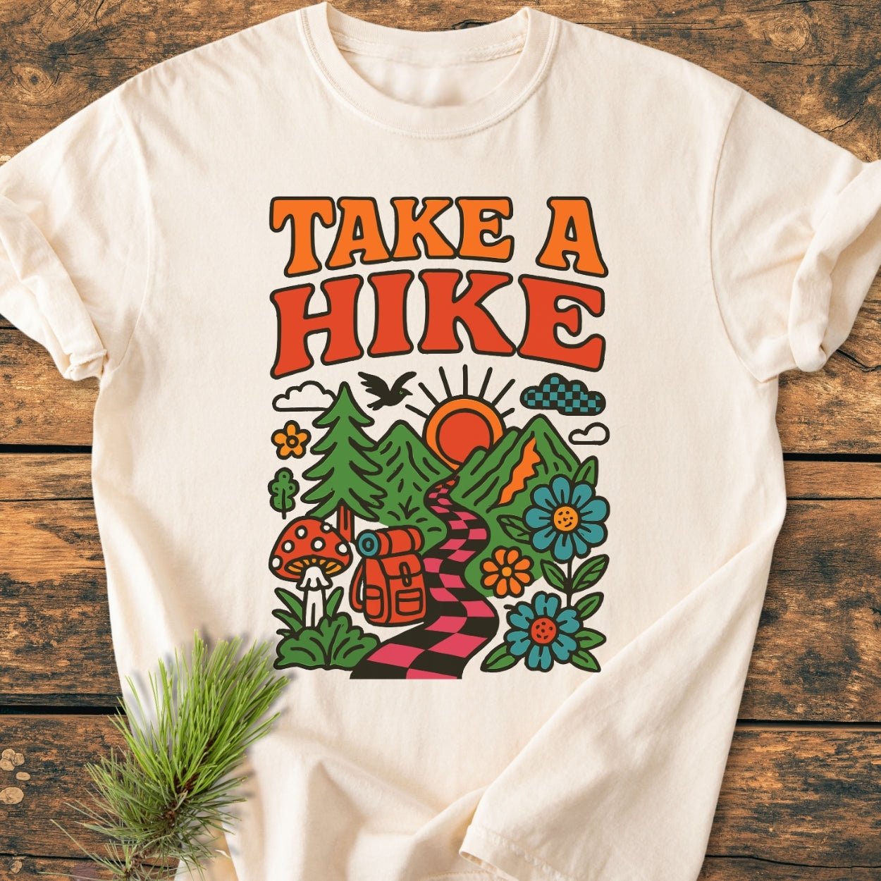 Take A Hike Funky - Vintage Wash Tee features a vibrant retro illustration with a winding trail, mountains, and nature elements. The slogan TAKE A HIKE is boldly printed in orange and red.
