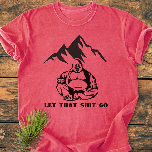 Let That Shit Go - Vintage Wash Tee features a black Buddha graphic and slogan on a heather-red shirt, laid on wood with pine sprig, showcasing its relaxed fit and soft-washed, durable fabric.