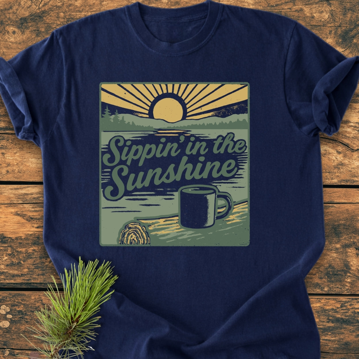 Sippin' In The Sunshine - Vintage Wash Tee features a retro outdoor scene with a sun, treeline, lake, and coffee mug, all on a navy-blue T-shirt, offering a relaxed fit and durable design.