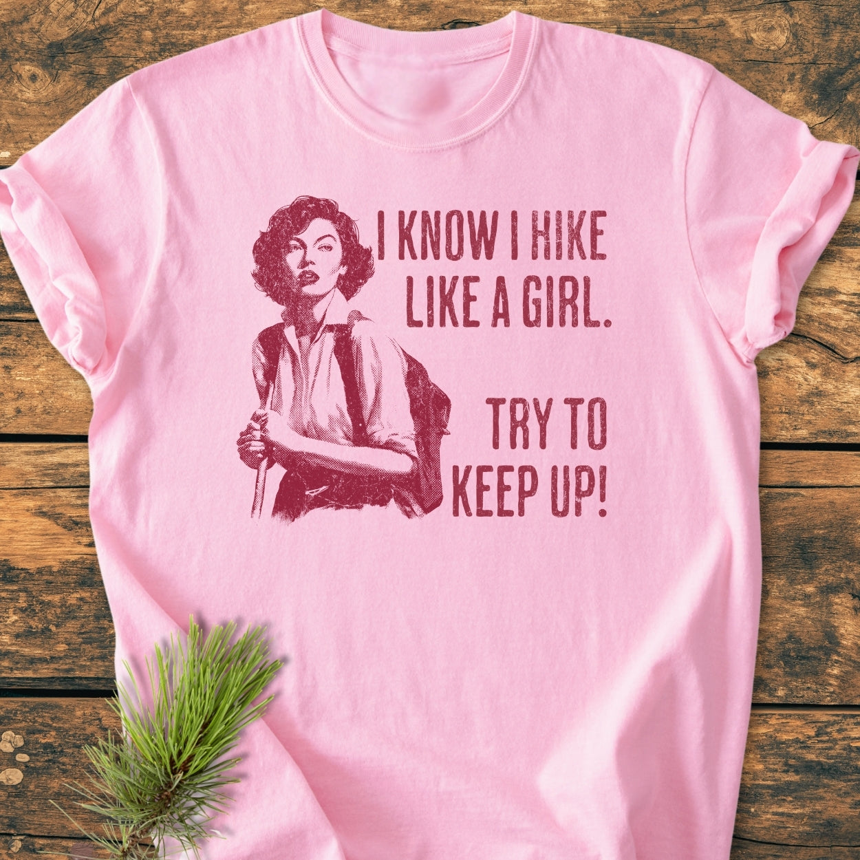 Hike Like A Girl - Vintage Wash Tee features a light-pink design with a vintage-style illustration of a woman hiker in dark red, highlighting the phrase, “I KNOW I HIKE LIKE A GIRL. TRY TO KEEP UP!”.