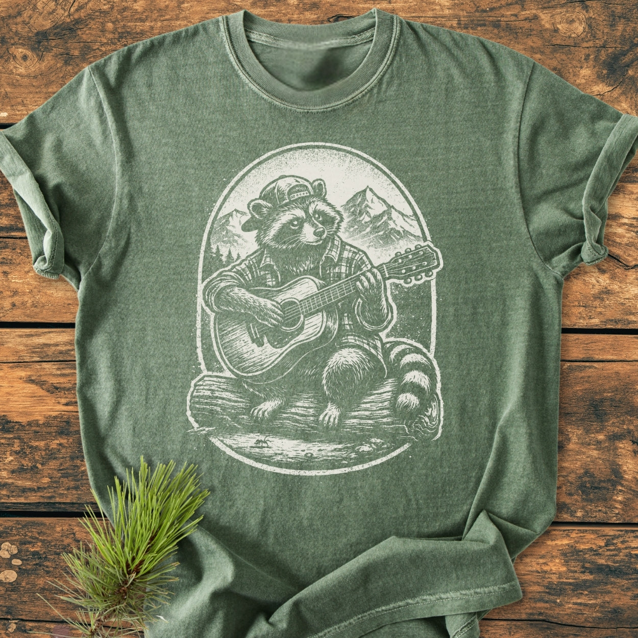 Guitar Playing Raccoon - Vintage Wash Tee features a raccoon illustration playing guitar on a green, short-sleeve T-shirt, offering a cozy, relaxed fit with durable, soft-washed 100% ring-spun cotton.