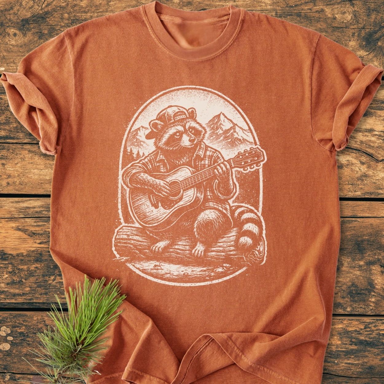 Guitar Playing Raccoon - Vintage Wash Tee features a raccoon illustration on a rust-colored shirt, highlighting a relaxed fit and durable design, perfect for everyday wear and available in multiple colors.