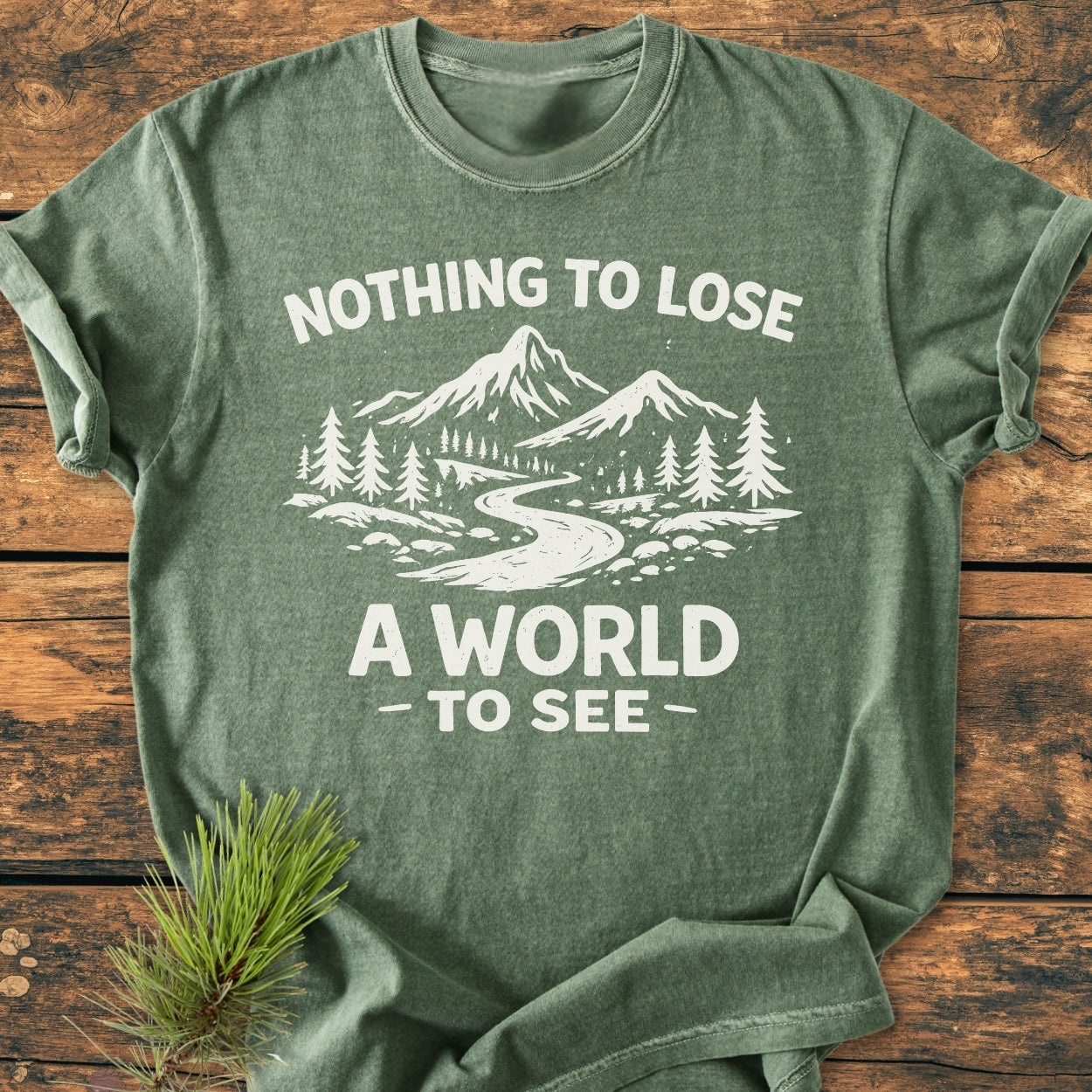 Nothing To Lose - Vintage Wash Tee in heather-green, featuring a white mountain-and-forest print with slogan, laid on wood. Includes a small pine sprig accentuating the nature theme.
