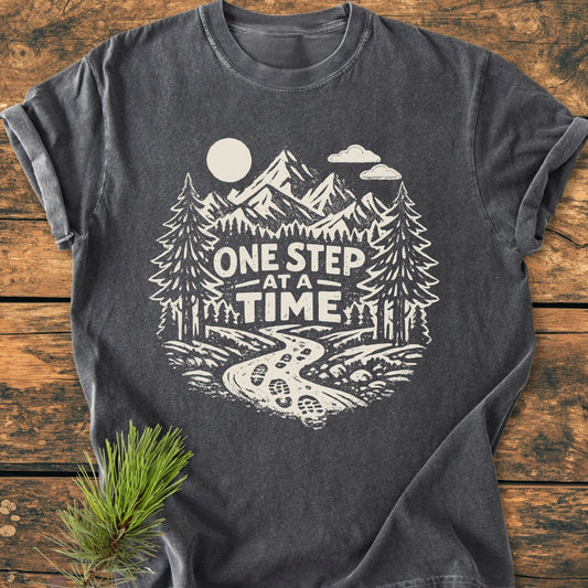 One Step At A Time - Vintage Wash Tee features a hand-drawn mountain scene with a motivational slogan on a charcoal-gray background, showcasing casual comfort and durability with its relaxed fit and soft 100% cotton fabric.