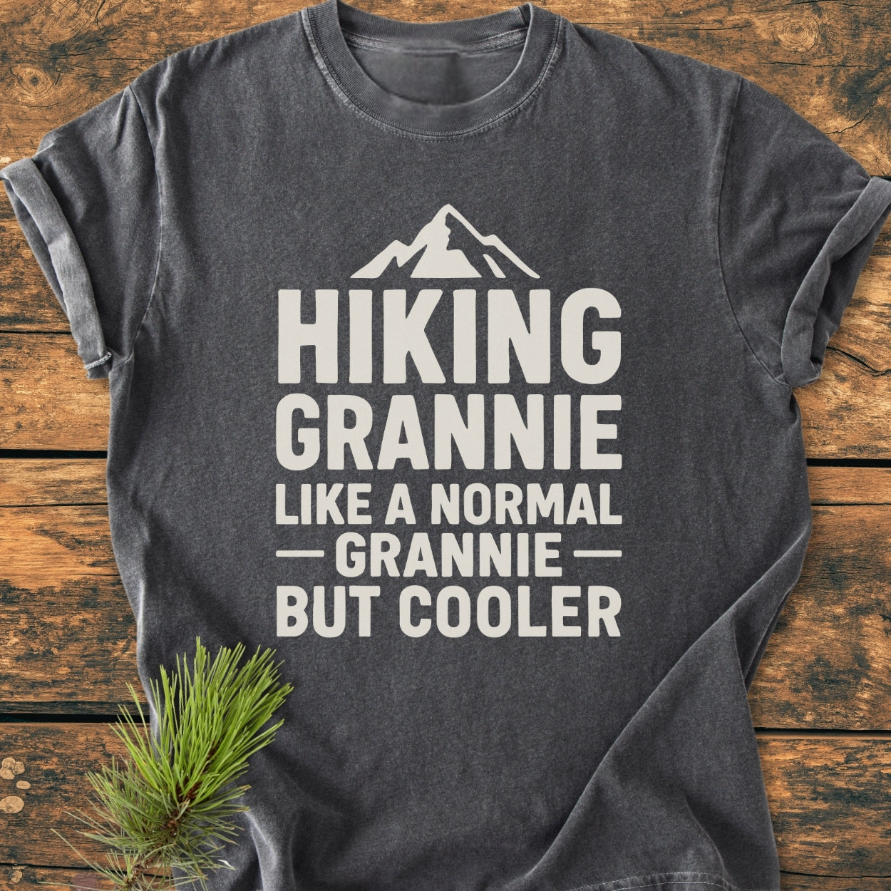 Hiking Grannie - Vintage Wash Tee: Dark-gray t-shirt with a stylized mountain and Hiking Grannie text, laid flat with a pine sprig accent. Made from soft, durable ring-spun cotton for everyday comfort.