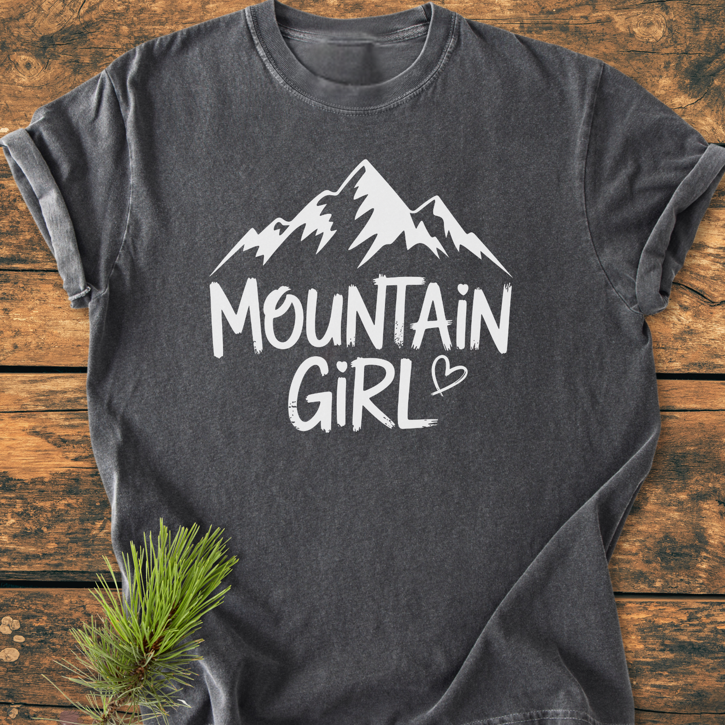 Charcoal-grey Mountain Girl - Vintage Wash Tee with a white mountain silhouette and text, laid flat on wood. Features soft-washed, garment-dyed fabric with a relaxed fit, highlighting comfort and durability.