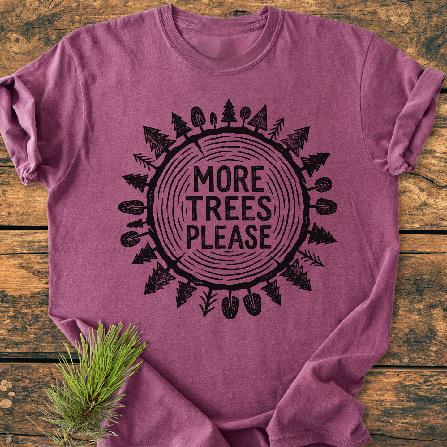 More Trees Please - Vintage Wash Tee with tree ring graphic, relaxed fit, 100% ring-spun cotton, displayed on wood surface with pine branch accent, showcasing comfort and style.