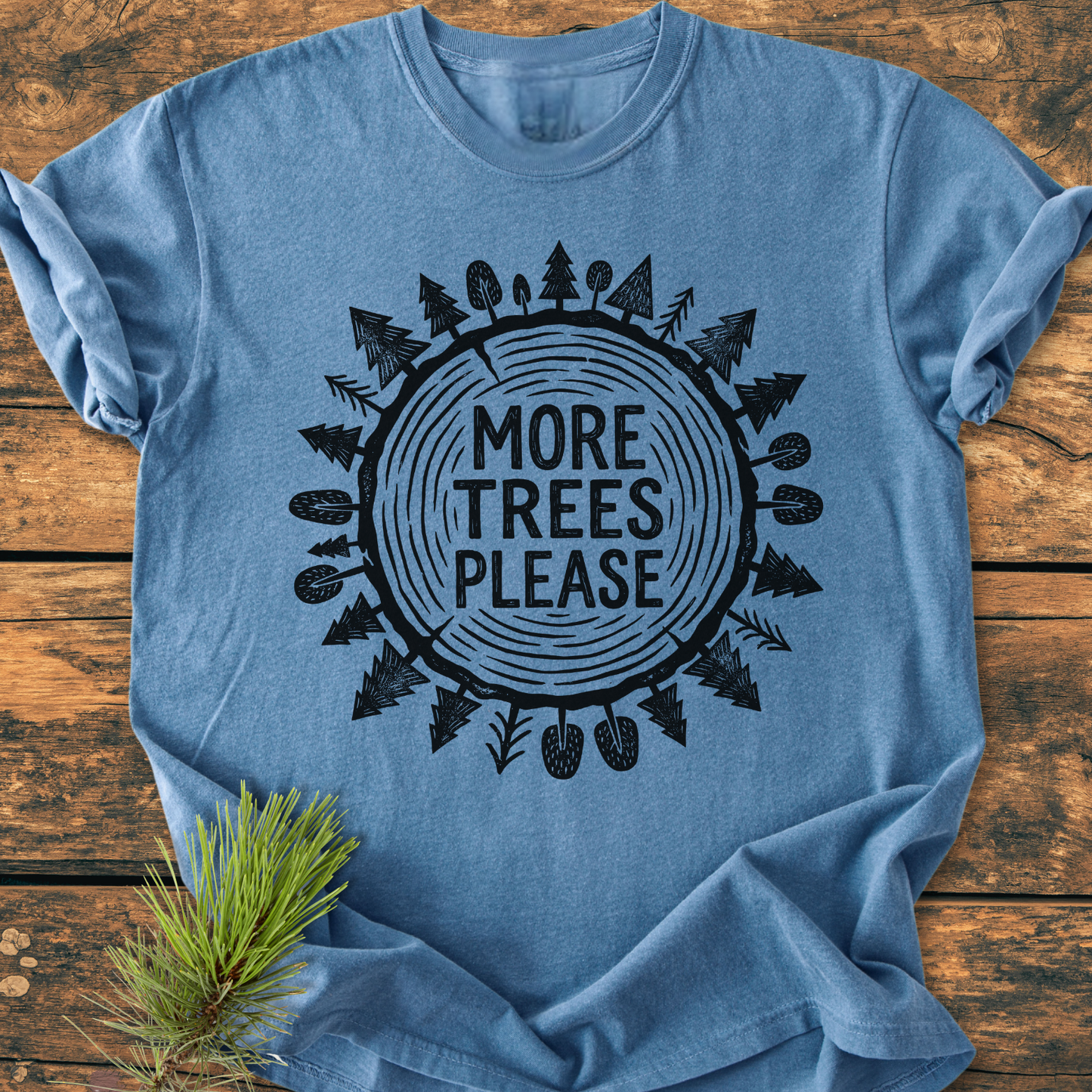 More Trees Please - Vintage Wash Tee featuring a tree-ring graphic with surrounding pine trees, laid flat with a pine sprig accent, highlighting its cozy, relaxed fit and durable garment-dyed fabric.