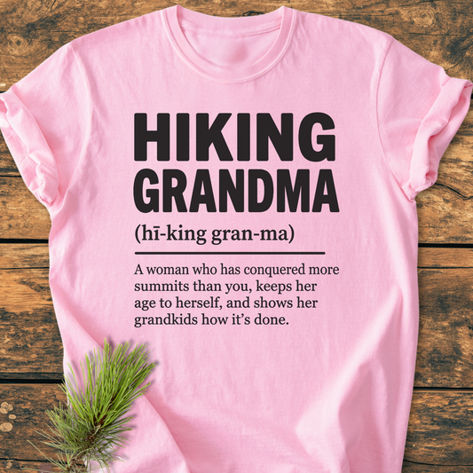 The Hiking Grandma Definition - Vintage Wash Tee features bold lettering and a playful definition, laid flat with pine needles on a wooden surface, showcasing its relaxed, durable design.