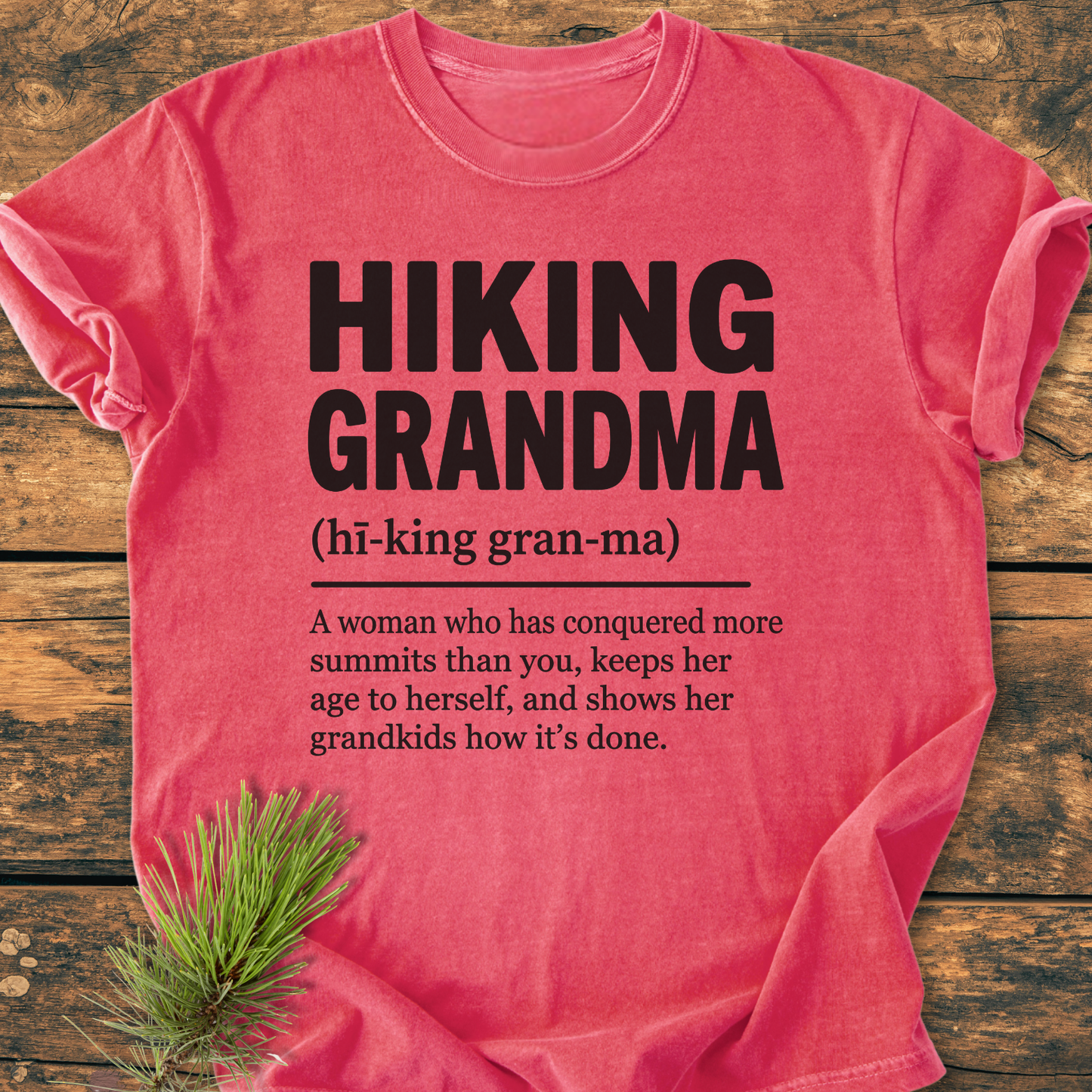 Hiking Grandma Definition - Vintage Wash Tee on rustic wood, featuring bold black text and playful definition. Soft-washed, ring-spun cotton with relaxed fit, ideal for active grandmas. Pine sprig accentuates the design.