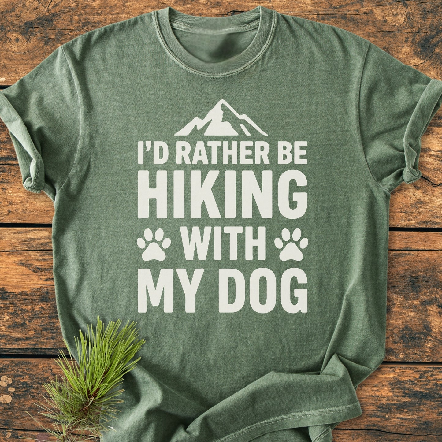 I'd Rather Be Hiking With My Dog - Vintage Wash Tee in heather-green, featuring bold white text with mountain and paw prints, styled with a pine sprig, showcasing its cozy, relaxed fit.