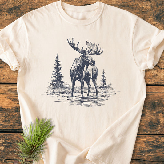 Moose - Vintage Wash Tee displayed flat on rustic wood, showcasing a detailed moose sketch with pine trees. Made from soft, pre-shrunk, garment-dyed cotton for comfort and durability.