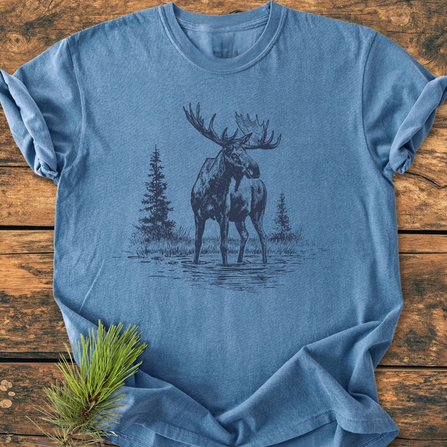 Moose - Vintage Wash Tee features a heather-blue, folded T-shirt with a bull moose illustration. Made from pre-shrunk, soft-washed, 100% ring-spun cotton for a relaxed, durable fit.