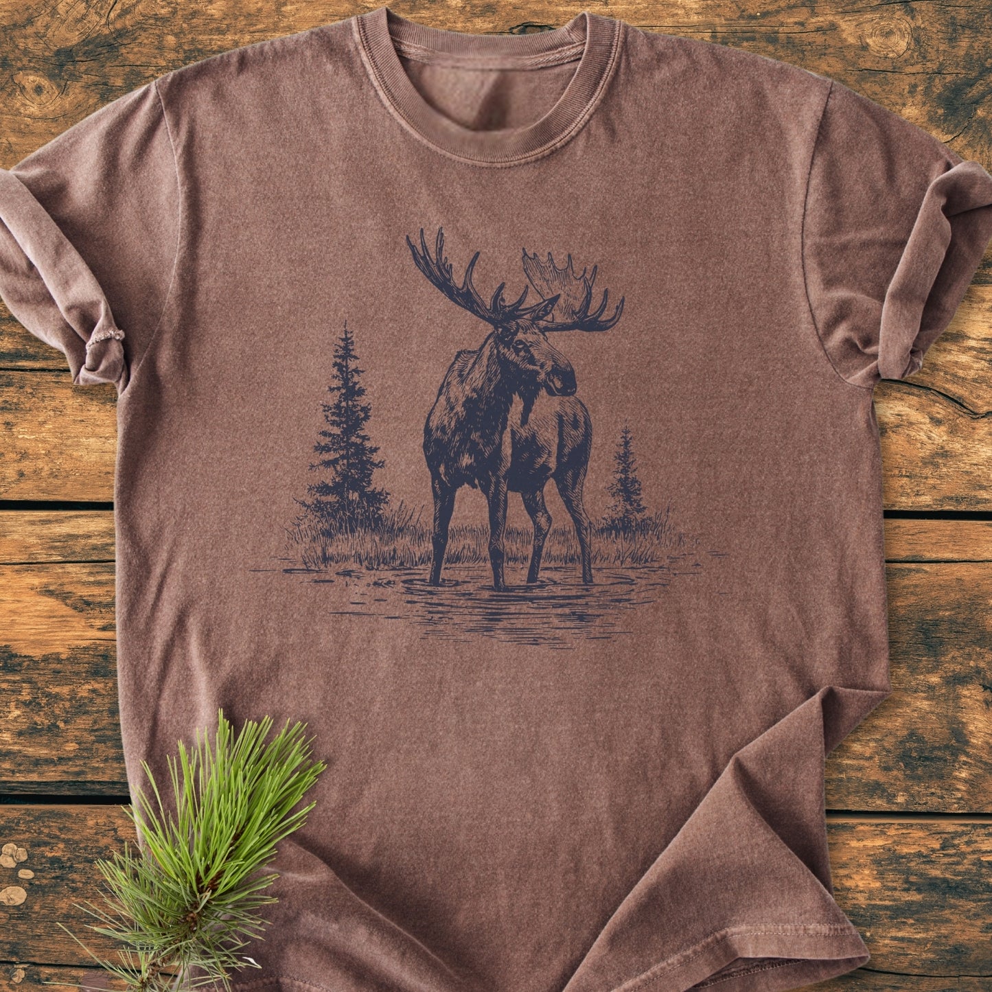 Moose - Vintage Wash Tee featuring a dark-ink bull moose sketch, laid on a wooden surface with a pine sprig; embodies Comfort Colors' soft, durable, 100% ring-spun cotton, garment-dyed t-shirt.