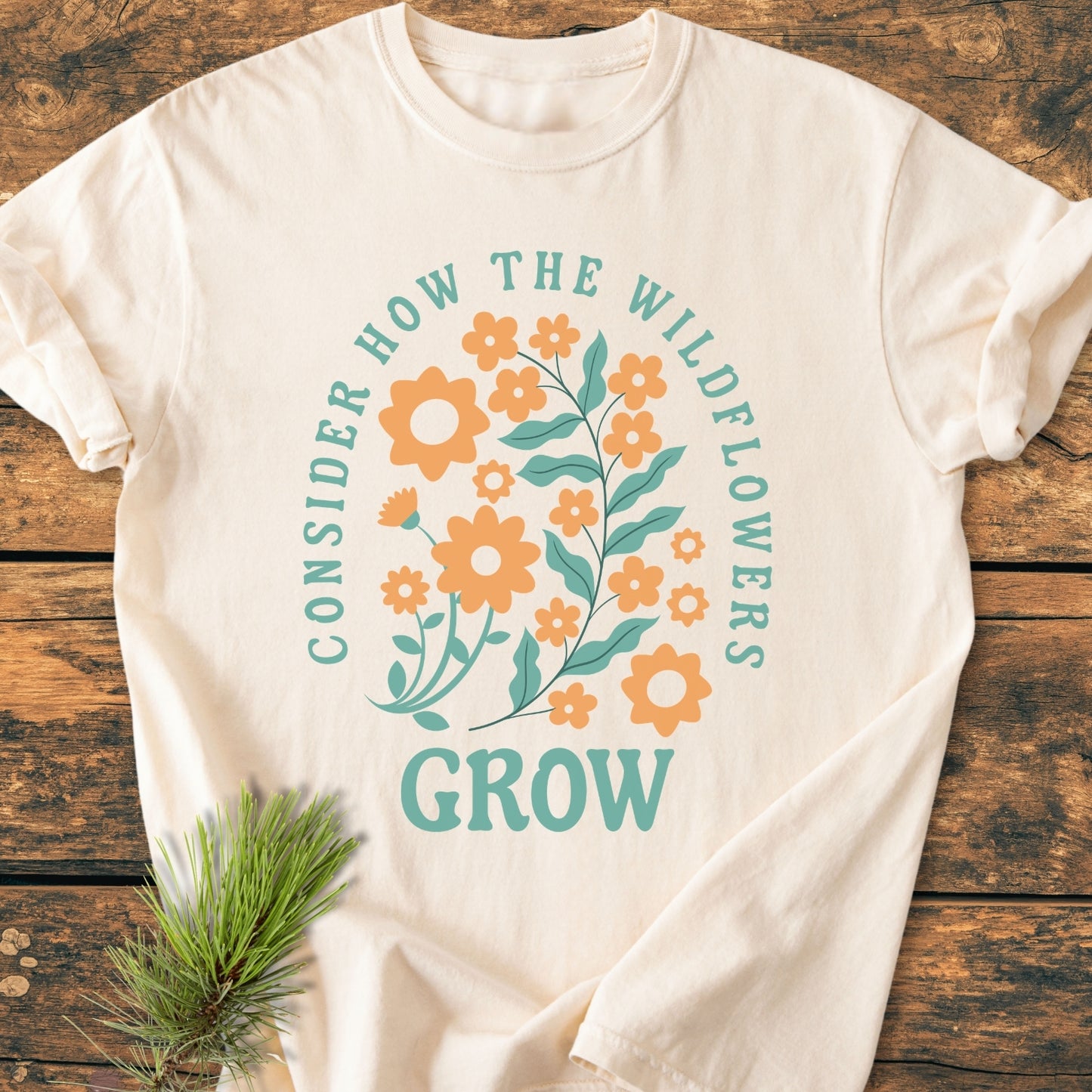 Wildflowers Luke 12,27 - Vintage Wash Tee features a wildflower graphic with CONSIDER HOW THE WILDFLOWERS and GROW text, laid on rustic wood, showcasing its relaxed, cozy fit.