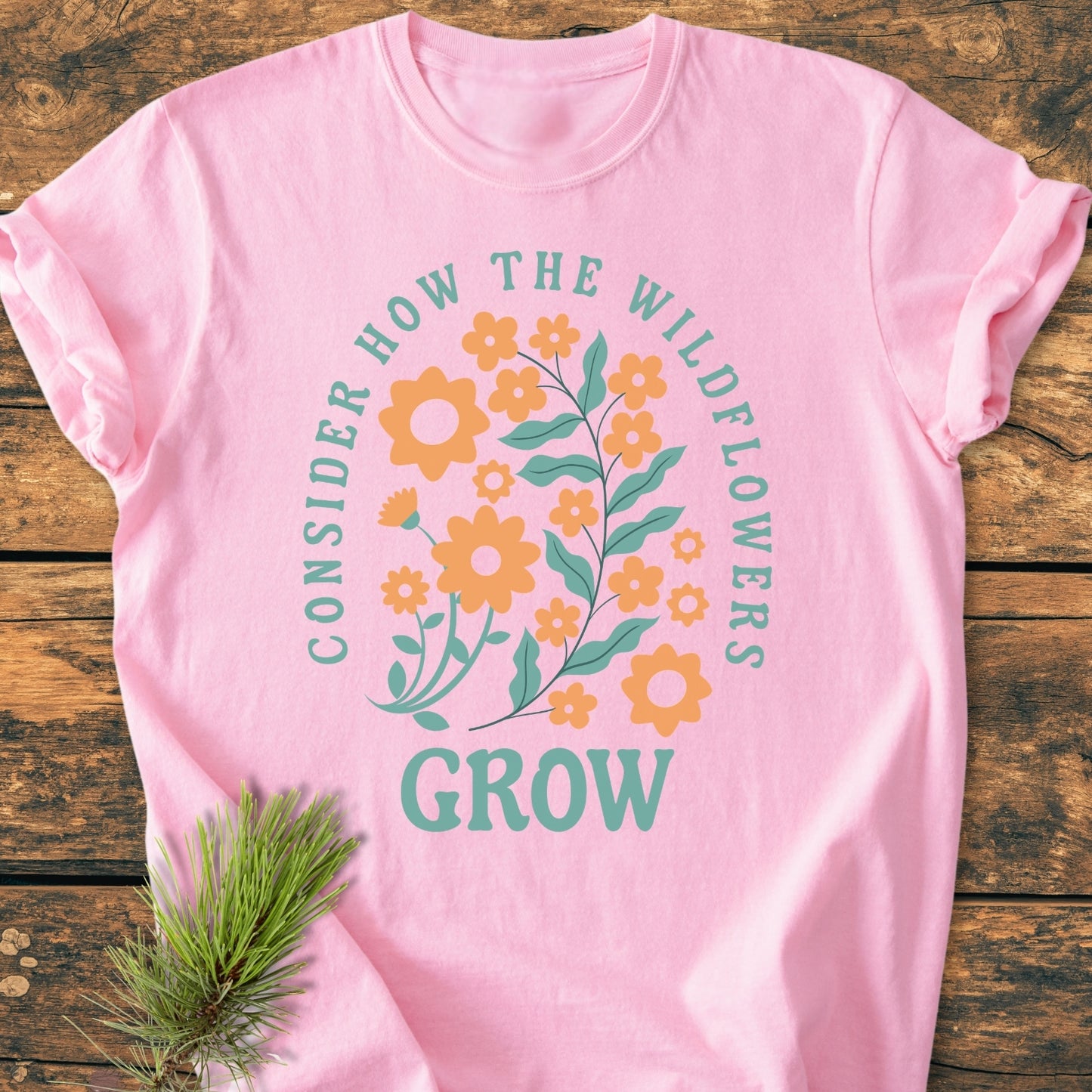 Wildflowers Luke 12,27 - Vintage Wash Tee features a floral graphic with CONSIDER HOW THE WILDFLOWERS GROW text. Laid on wood, highlighting soft fabric and relaxed fit.
