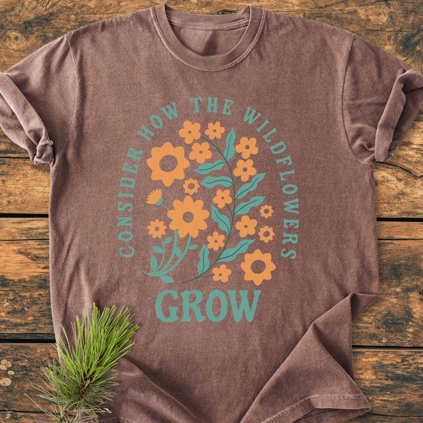 Wildflowers Luke 12,27 - Vintage Wash Tee features a wildflower bouquet print with inspirational text. Laid on a rustic wooden surface, this Comfort Colors tee offers cozy style and durability.