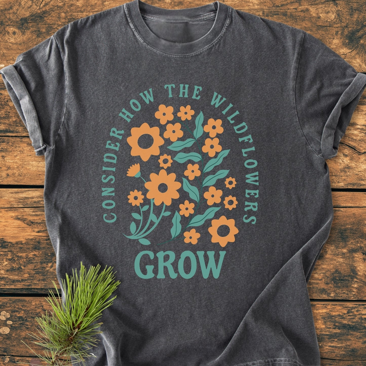 Wildflowers Luke 12,27 - Vintage Wash Tee features a colorful wildflower graphic and inspirational text. The charcoal-grey T-shirt, with rolled sleeves and a pine sprig accent, offers a relaxed, cozy fit.
