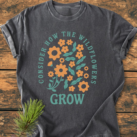 Wildflowers Luke 12,27 - Vintage Wash Tee features a colorful wildflower graphic and inspirational text. The charcoal-grey T-shirt, with rolled sleeves and a pine sprig accent, offers a relaxed, cozy fit.
