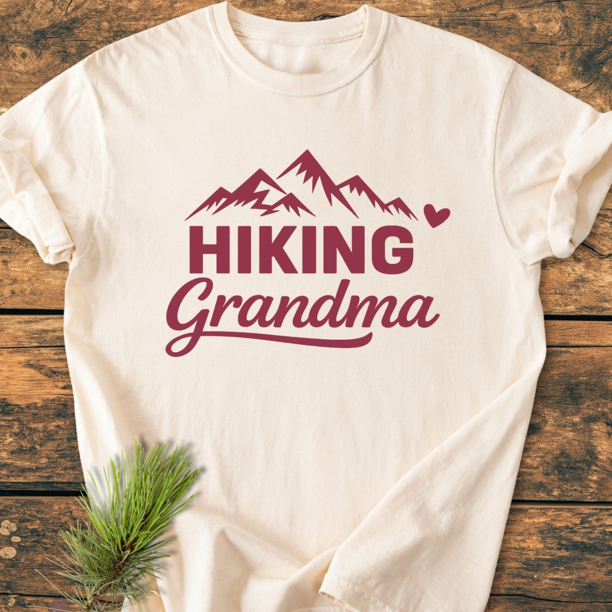 Hiking Grandma - Vintage Wash Tee featuring mountain peaks and text design, laid on wood. Soft-washed, garment-dyed, 100% cotton for comfort and durability, ideal for casual wear.