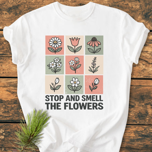 Stop And Smell The Flowers - Vintage Wash Tee features nine pastel floral squares and bold slogan on a white T-shirt, laid on wood with a pine sprig, showcasing relaxed, durable comfort.