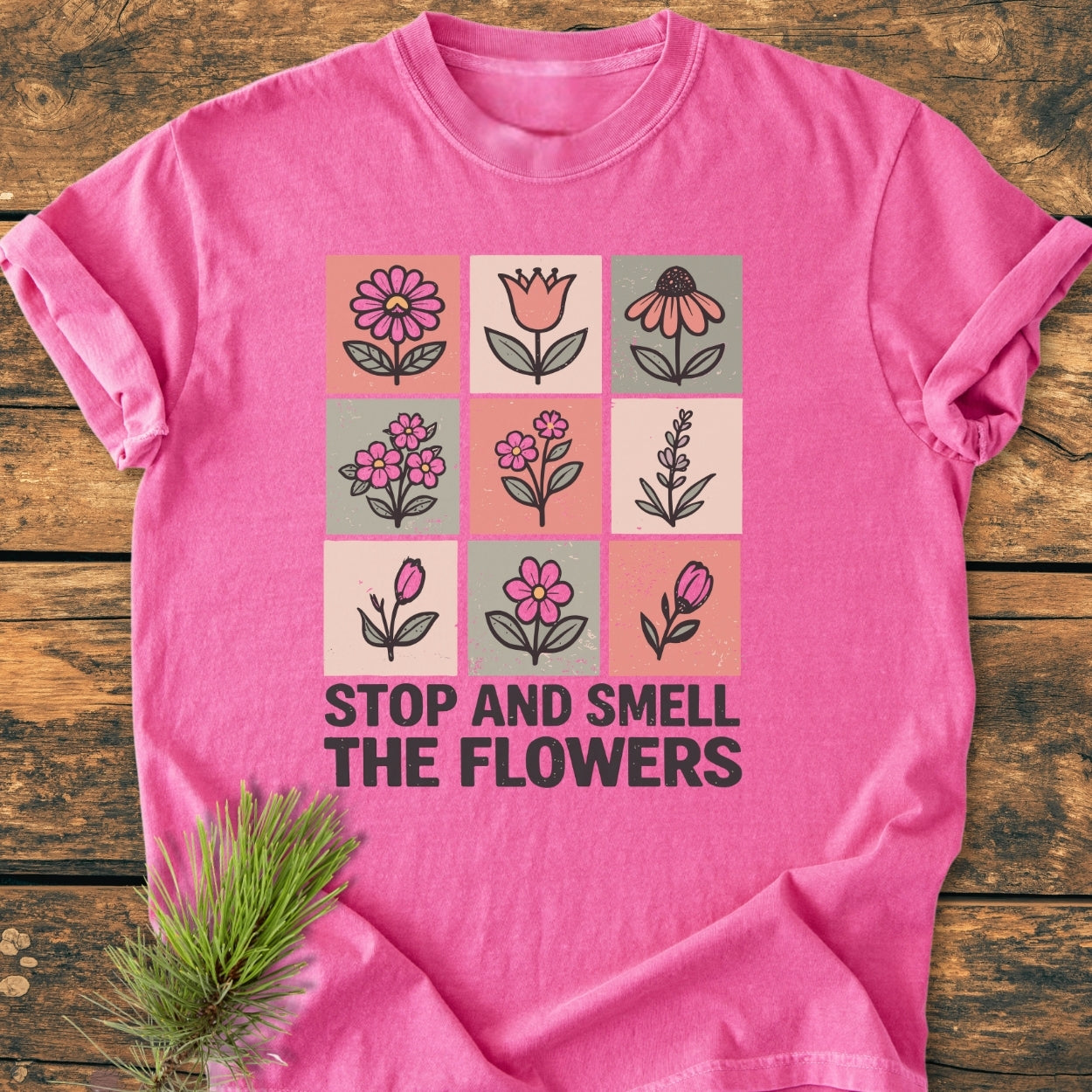 Stop And Smell The Flowers - Vintage Wash Tee: A pink T-shirt with nine floral panels and a slogan, styled on rustic wood with a pine sprig, highlighting its cozy, durable design.