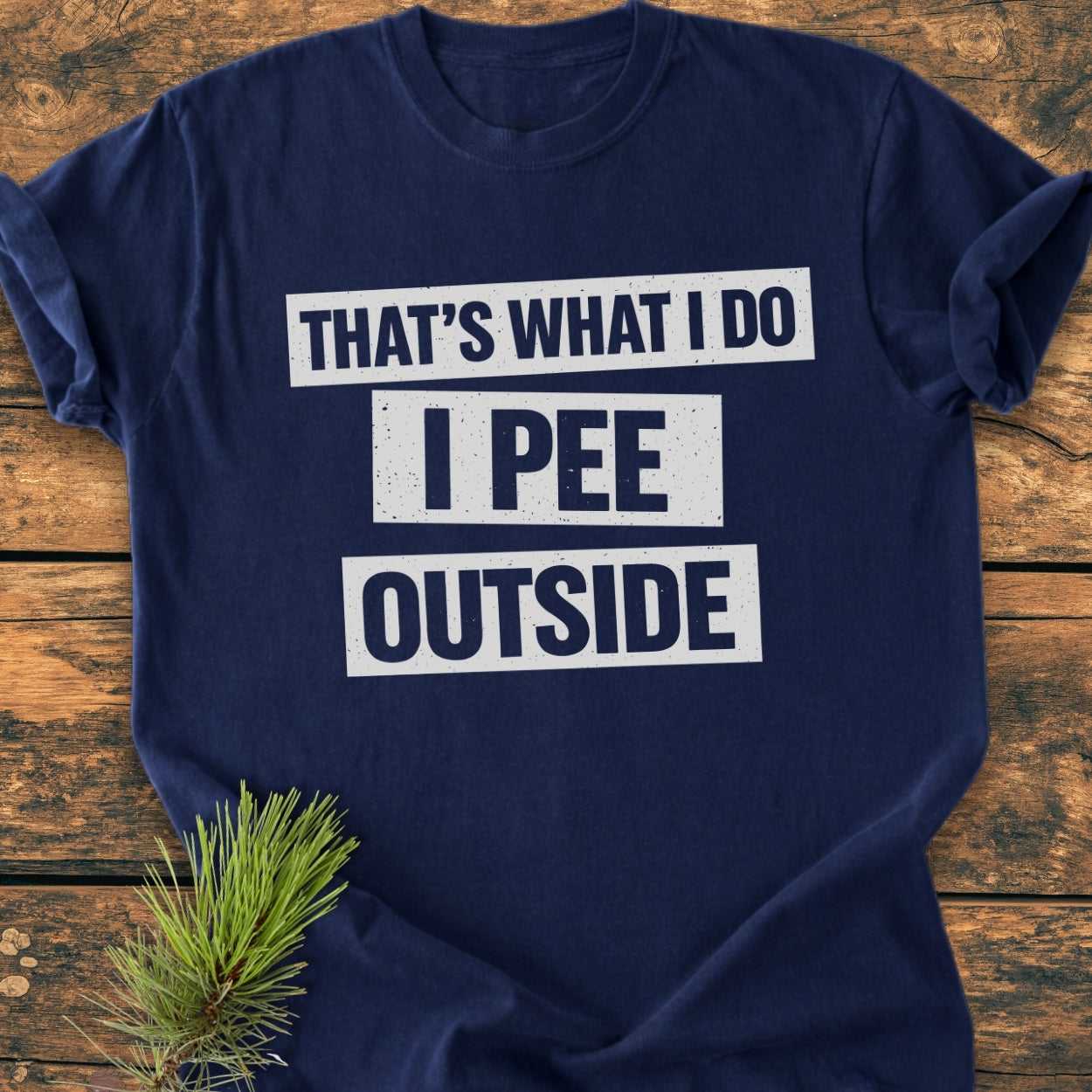 Navy-blue That's What I Do. I Pee Outside - Vintage Wash Tee with bold white slogan, laid flat on rustic wood, pine sprig accent. Comfortable, relaxed fit, garment-dyed cotton, durable stitching.