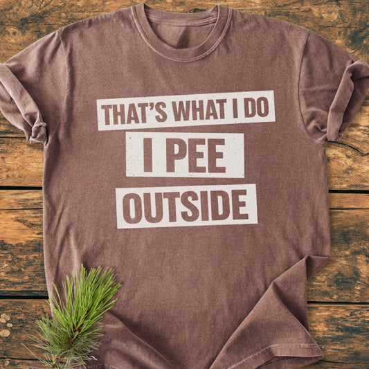 That's What I Do. I Pee Outside - Vintage Wash Tee, brownish, laid flat on wood; features bold text slogan, accompanied by a pine sprig, showcasing its rustic appeal and relaxed fit.