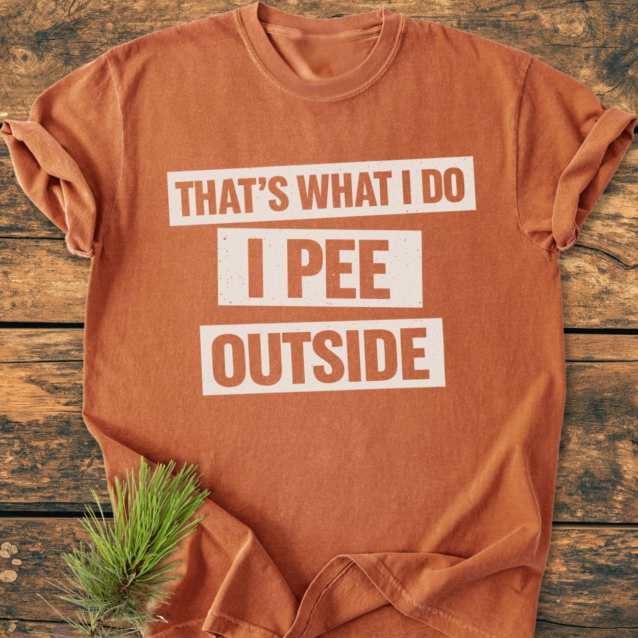 That's What I Do. I Pee Outside - Vintage Wash Tee on weathered wood, showcasing bold white slogan. Soft-washed, relaxed fit, 100% ring-spun cotton with pine needle accent for rustic appeal.