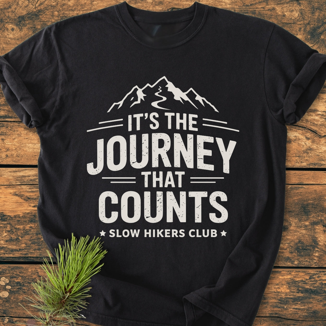 It's The Journey That Counts - Vintage Wash Tee features a white mountain-and-trail graphic and slogan on a black T-shirt, laid out on wood, conveying adventure and comfort.