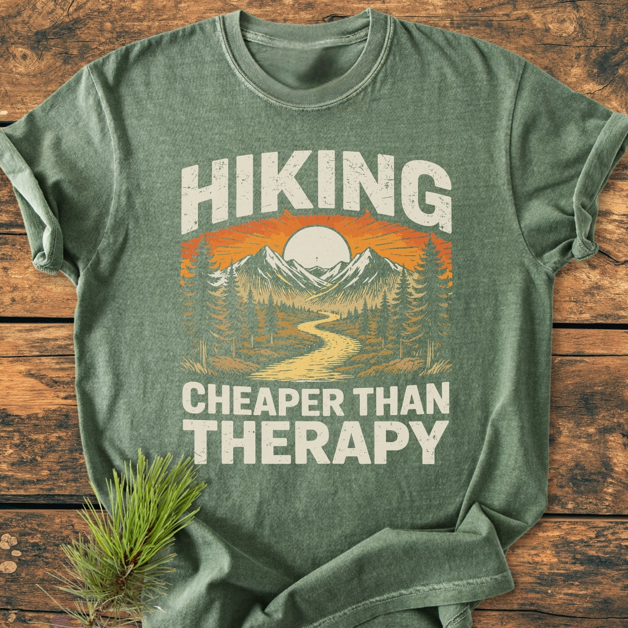 Hiking Cheaper Than Therapy - Vintage Wash Tee features a stylized outdoor scene with sun, mountains, and pine trees. Made from soft, ring-spun cotton, it offers a relaxed fit with durable stitching.