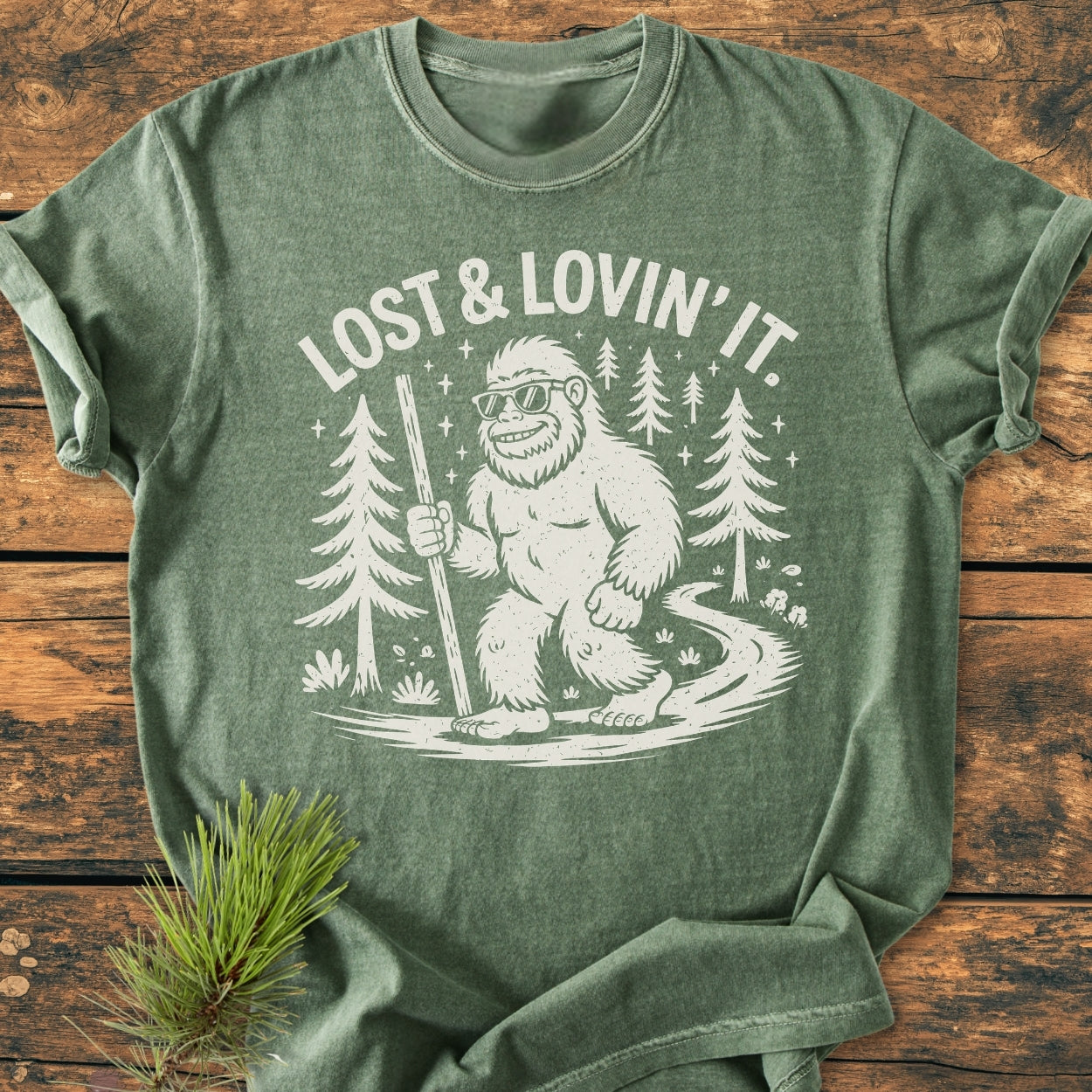 Lost And Lovin' It - Vintage Wash Tee features a Bigfoot line-art graphic with sunglasses, walking stick, and forest path, printed on a relaxed-fit, garment-dyed T-shirt, emphasizing comfort and durability.