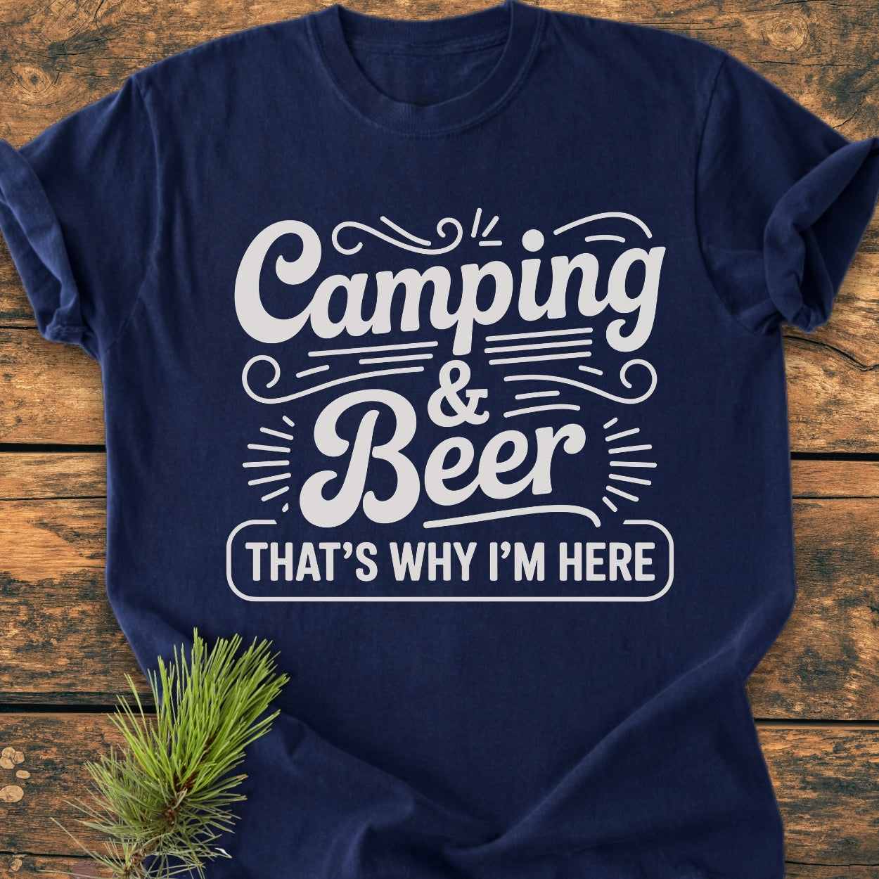 Navy-blue Camping And Beer - Vintage Wash Tee with white lettering and decorative accents, laid flat. Pine needles by the hem suggest a camping theme, highlighting its outdoorsy appeal.