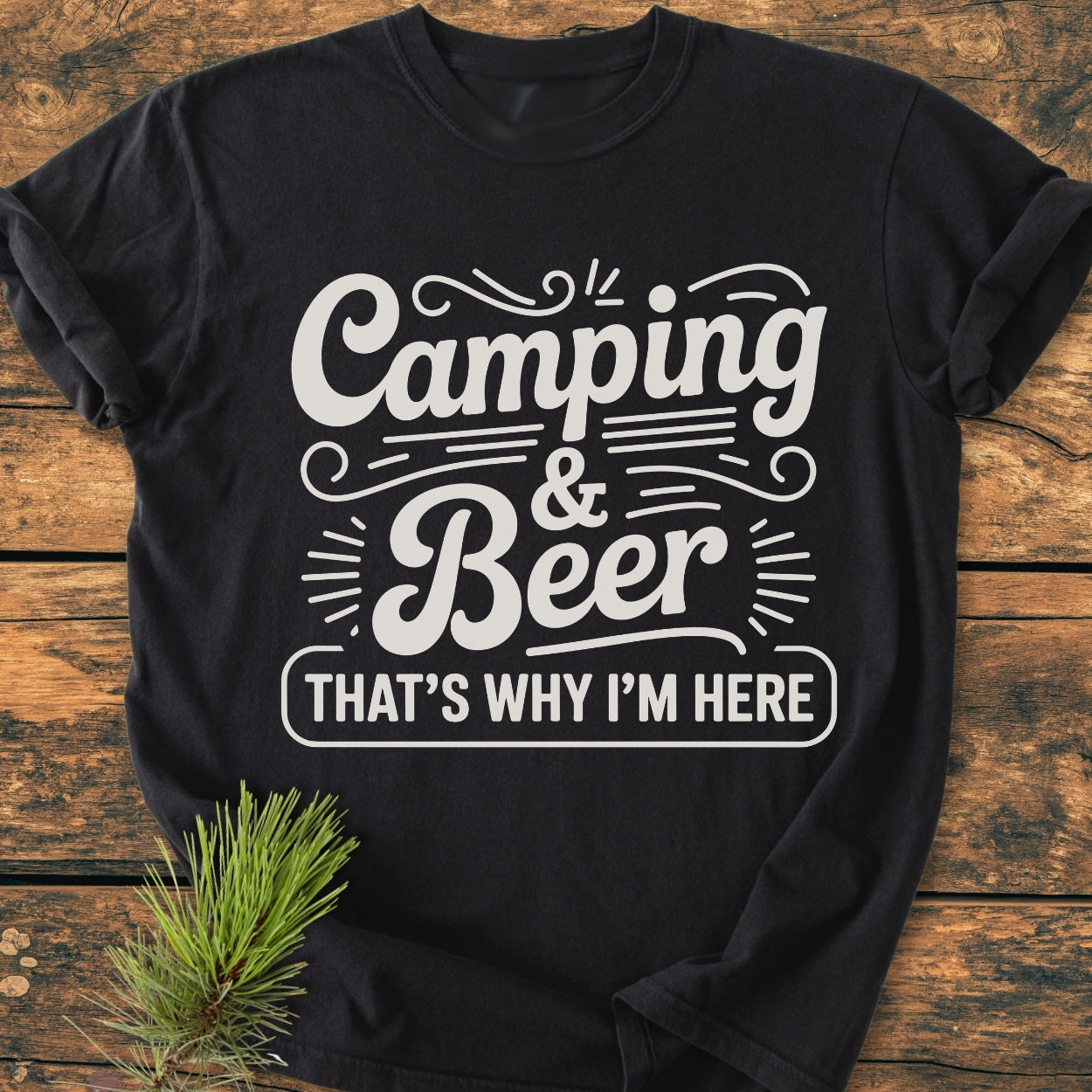 Camping And Beer - Vintage Wash Tee displayed flat with a bold white graphic on a wooden surface, featuring a pine sprig accentuating its camping theme. Perfect for relaxed, durable outdoor wear.