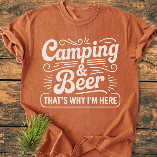 Camping And Beer - Vintage Wash Tee laid flat, showcasing the slogan Camping & Beer That’s Why I’m Here in white. Sprig of pine accentuates the rustic feel, highlighting its casual, relaxed design.