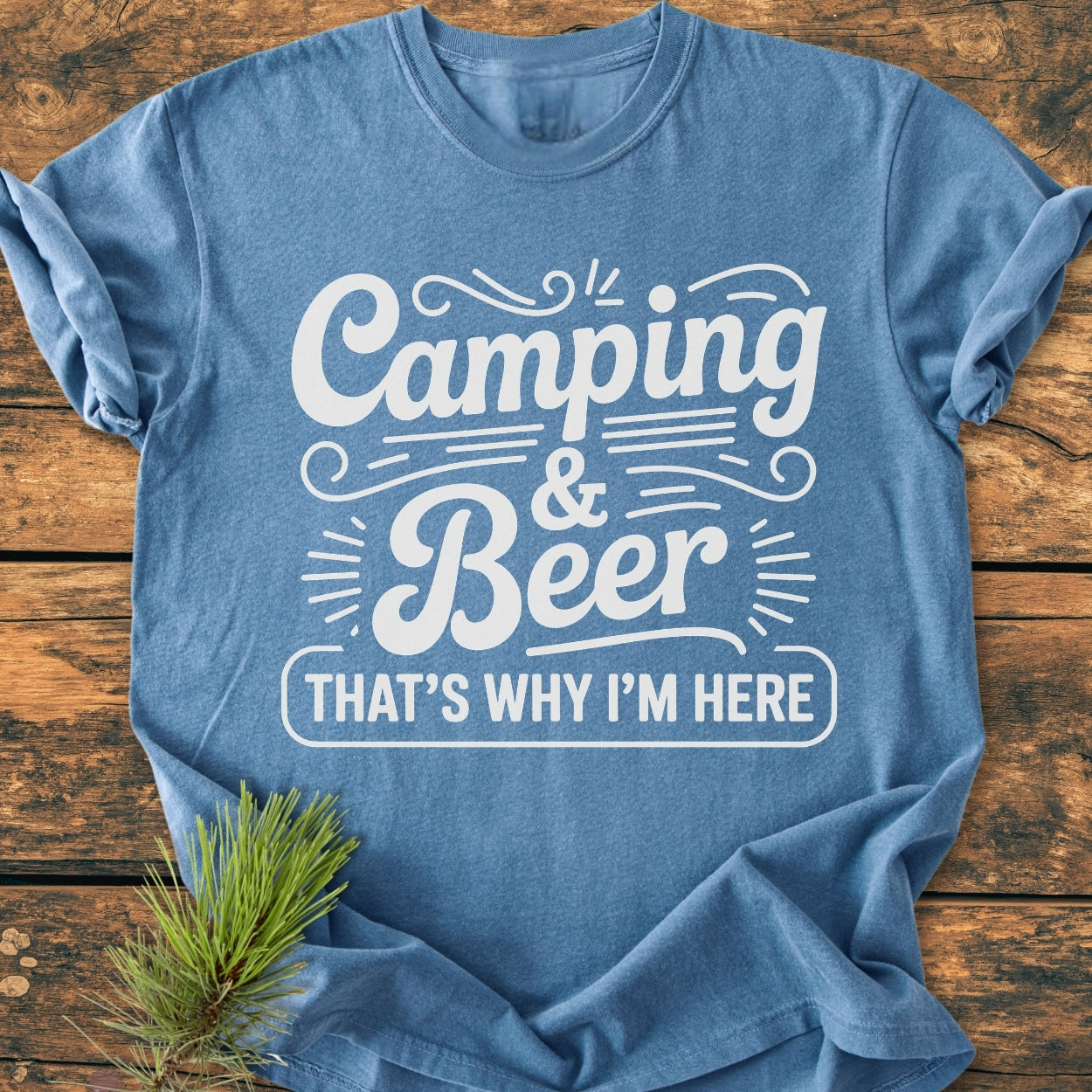 Heather-blue Camping And Beer - Vintage Wash Tee on rustic wood, with Camping & Beer That’s Why I’m Here in white. Pine needles accent the lower left corner.