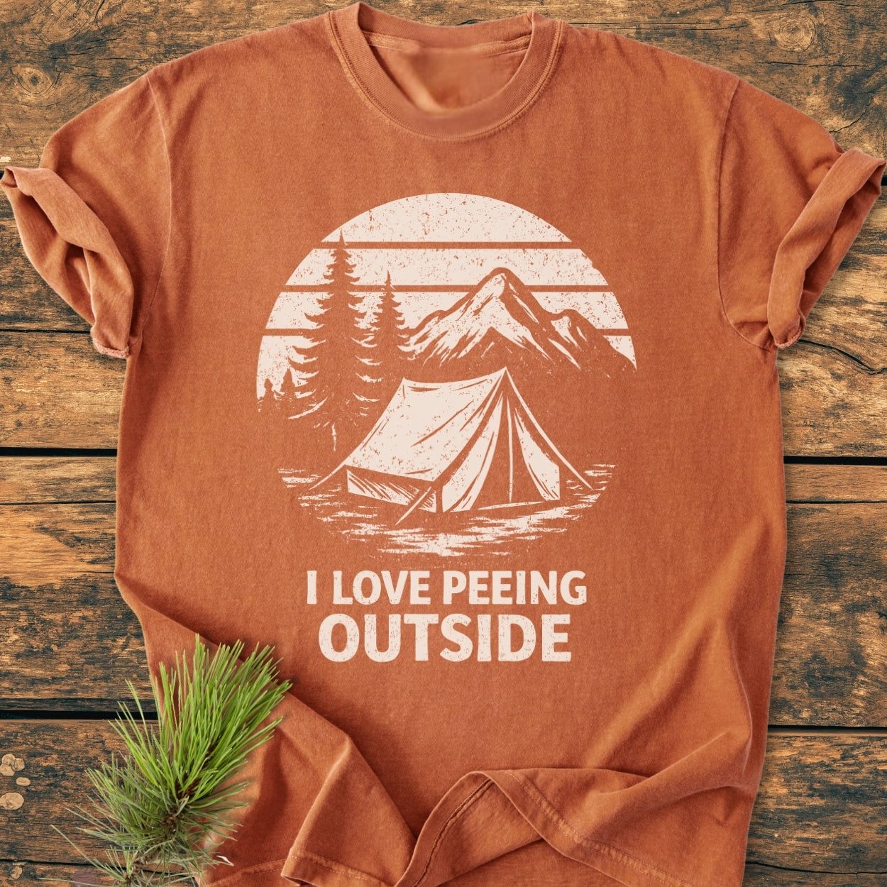 I LOVE Peeing Outside - Vintage Wash Tee features a rust-orange hue with a campsite graphic. Crafted from soft, garment-dyed ring-spun cotton, it offers a relaxed fit and durable double-needle stitching.
