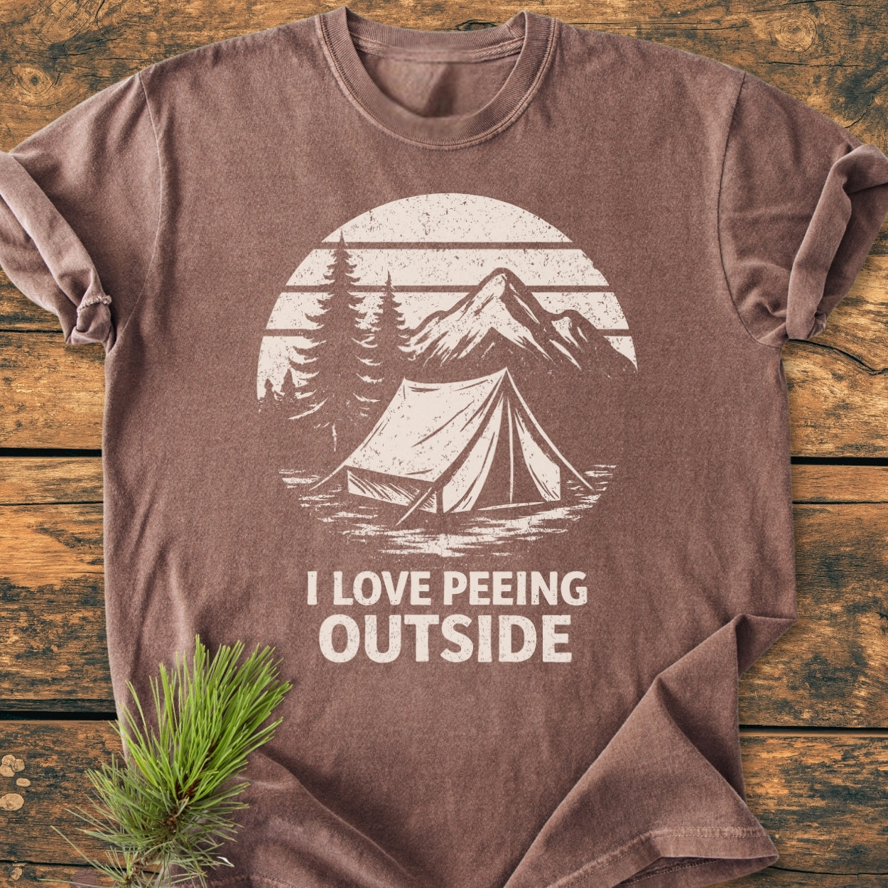 Brown I LOVE Peeing Outside - Vintage Wash Tee on rustic wood, featuring a white campsite graphic with trees and mountains. Made from soft, pre-shrunk 100% ring-spun cotton for relaxed comfort.