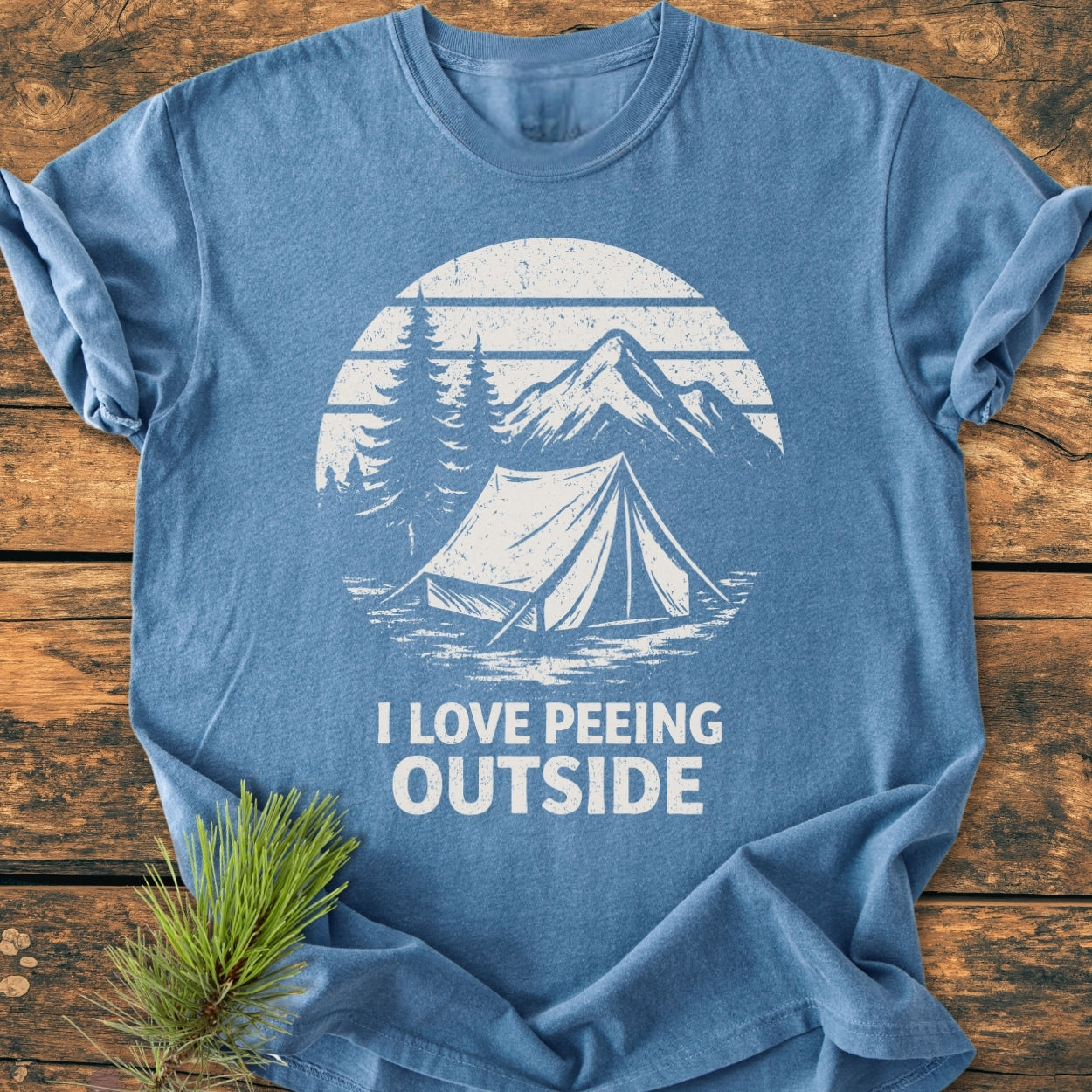 I LOVE Peeing Outside - Vintage Wash Tee: Blue T-shirt featuring a rustic graphic with a tent, pine trees, and mountains, plus the humorous phrase. Laid flat, showcasing its relaxed, durable construction.