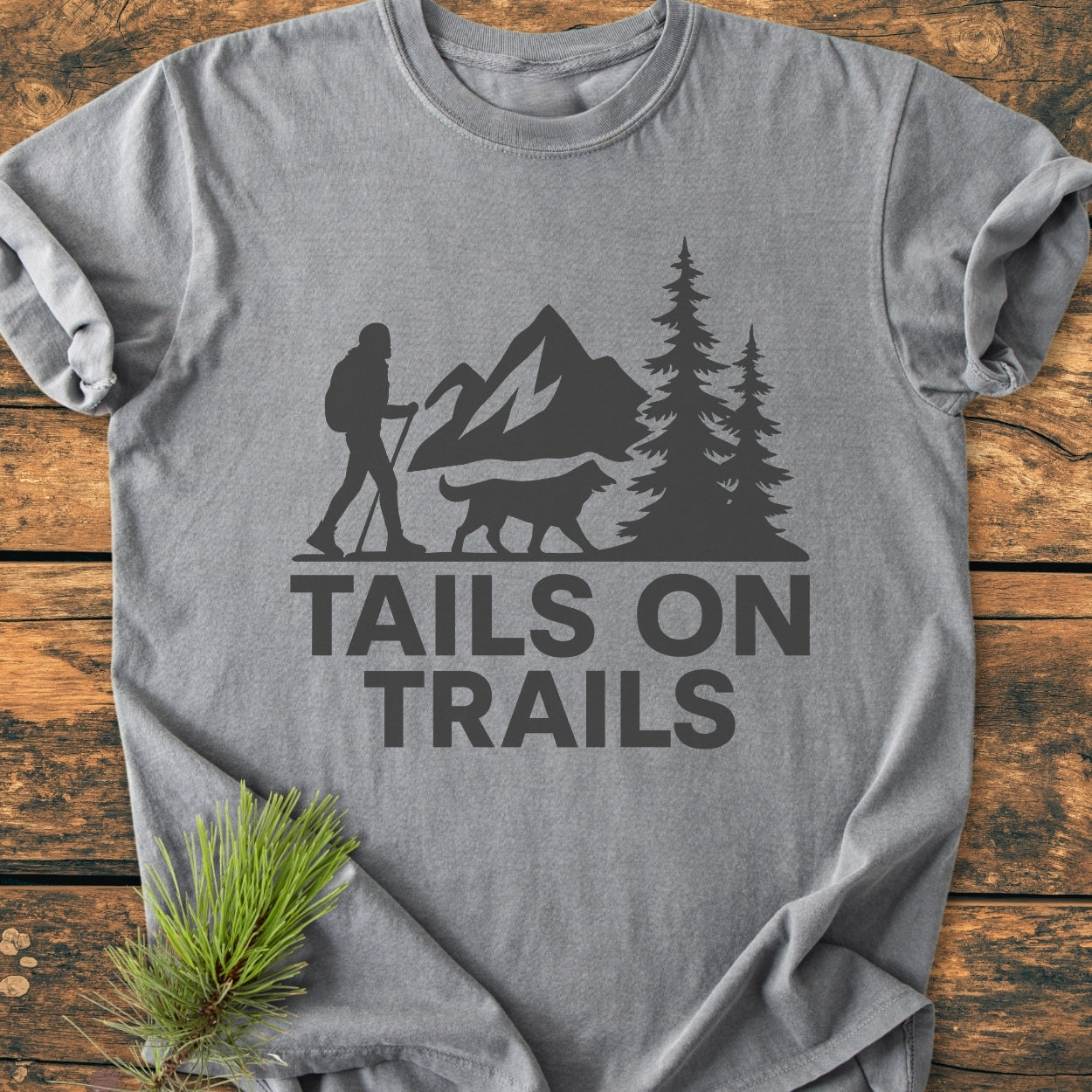 Tails On Trails - Vintage Wash Tee features a silhouette of a hiker and dog against mountains and trees, printed on a heather-gray T-shirt, offering comfort with its relaxed fit and durable construction.