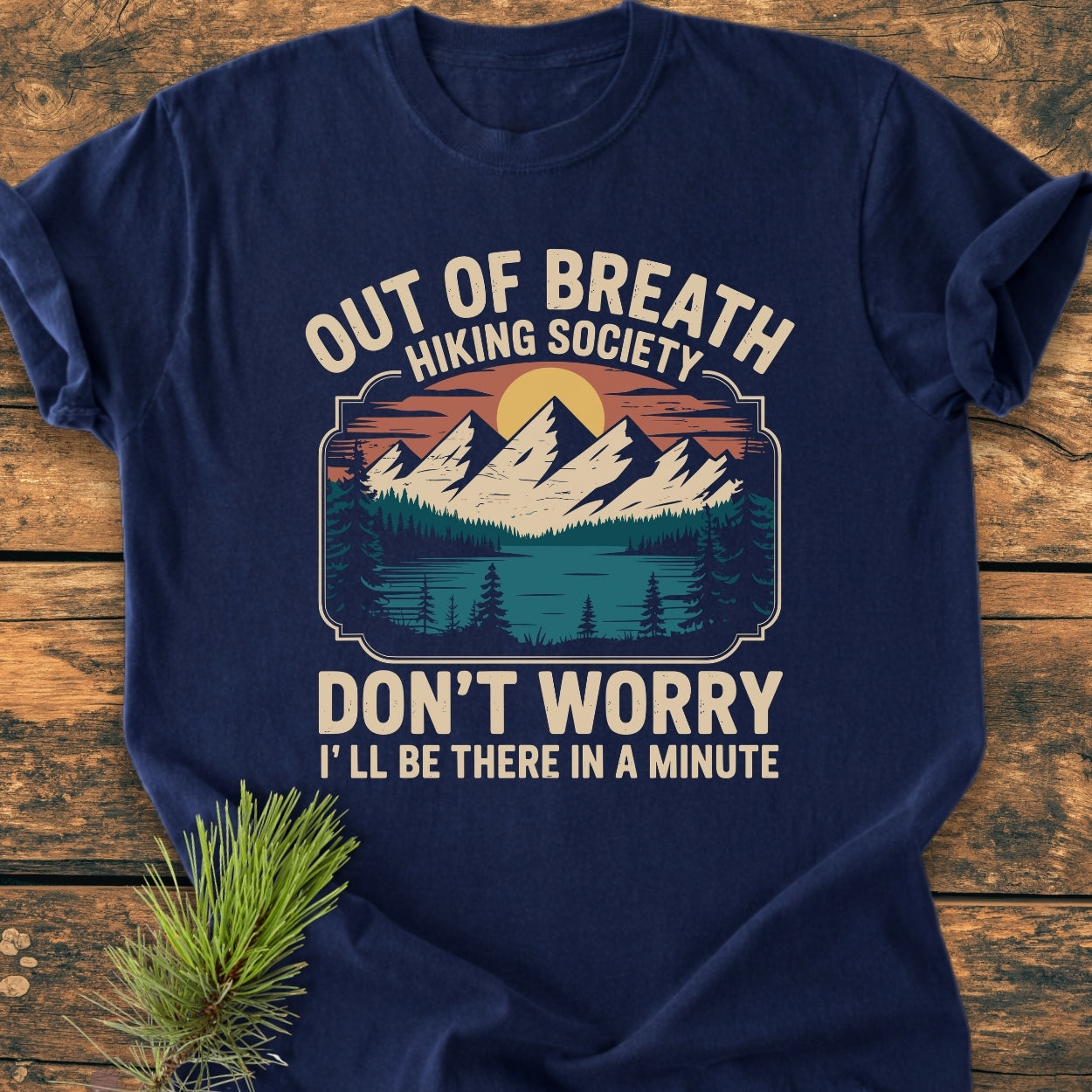 Out Of Breath Hiking Society - Vintage Wash Tee features a graphic of mountains and trees at sunset. The navy-blue tee offers a relaxed fit, ideal for daily wear with its soft, durable cotton fabric.