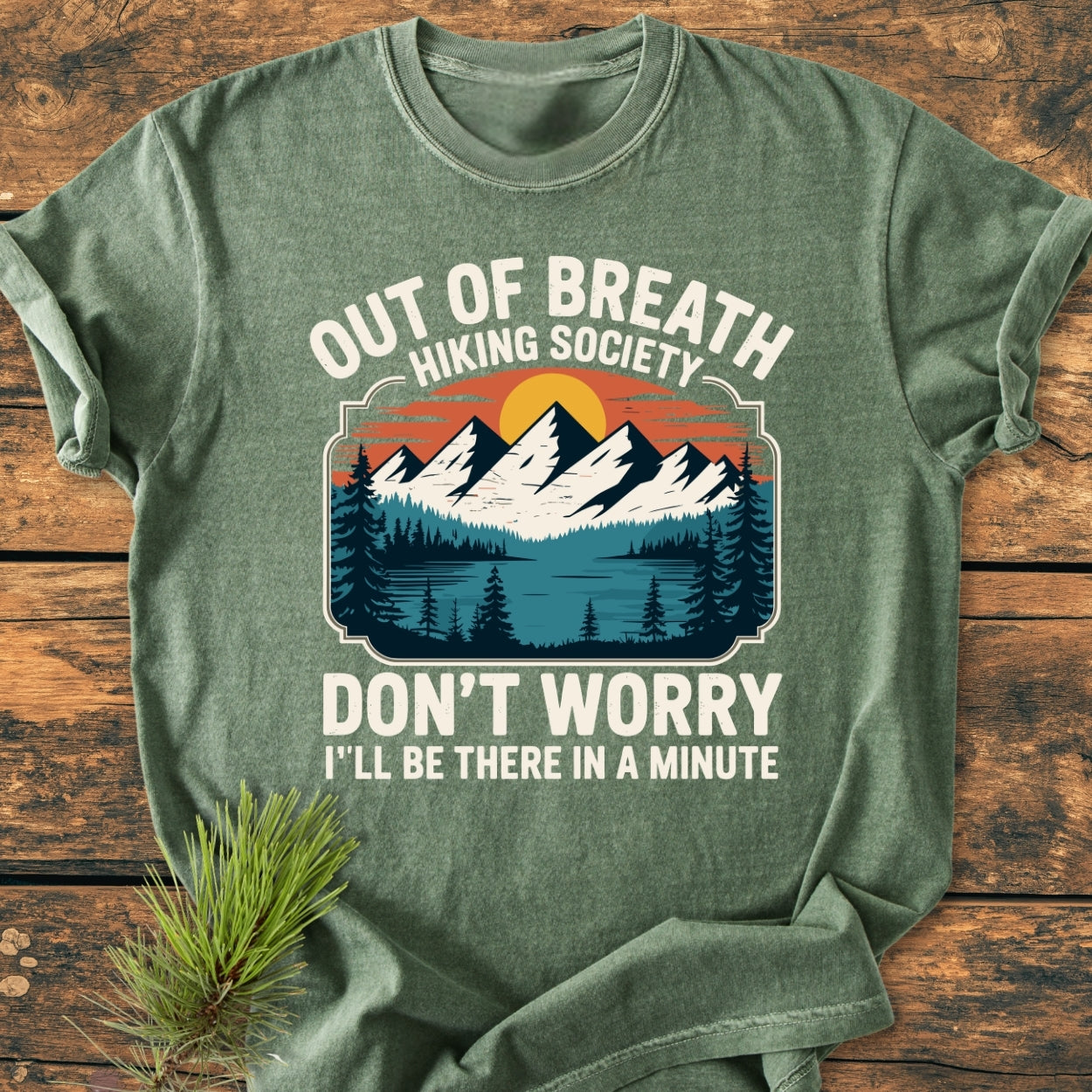 Out Of Breath Hiking Society - Vintage Wash Tee features a forest-green shirt with a stylized outdoor scene graphic, including mountains and a lake, and humorous text emphasizing a relaxed hiking vibe.