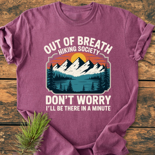 Out Of Breath Hiking Society - Vintage Wash Tee displayed flat; features a mountain graphic with snowy peaks, pine trees, and playful text in white, teal, and orange on a maroon background.