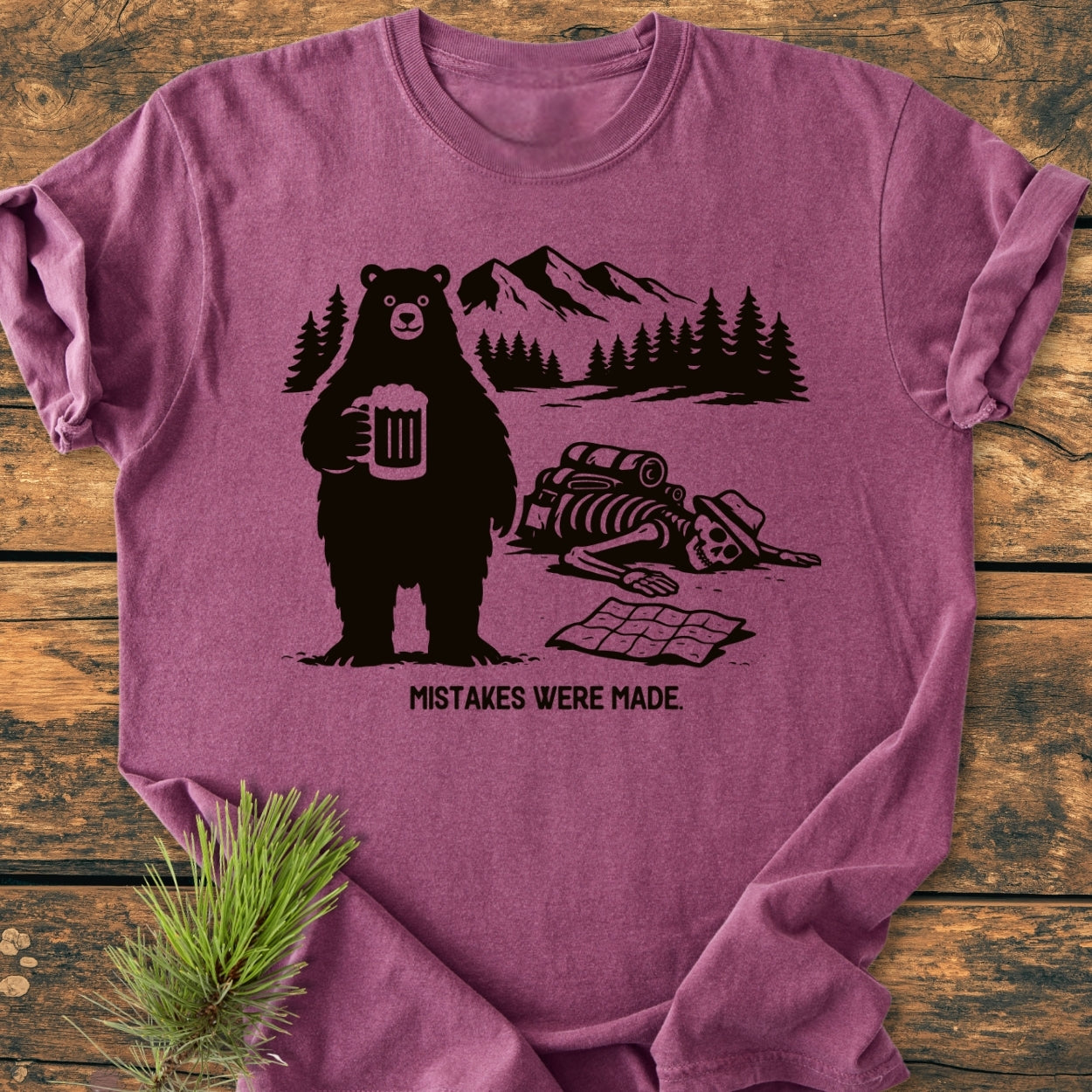 Mistakes Were Made - Vintage Wash Tee features a cartoon bear with a beer and a hiker’s skeleton in a forest scene, captioned humorously, on a soft, relaxed-fit 100% cotton tee.