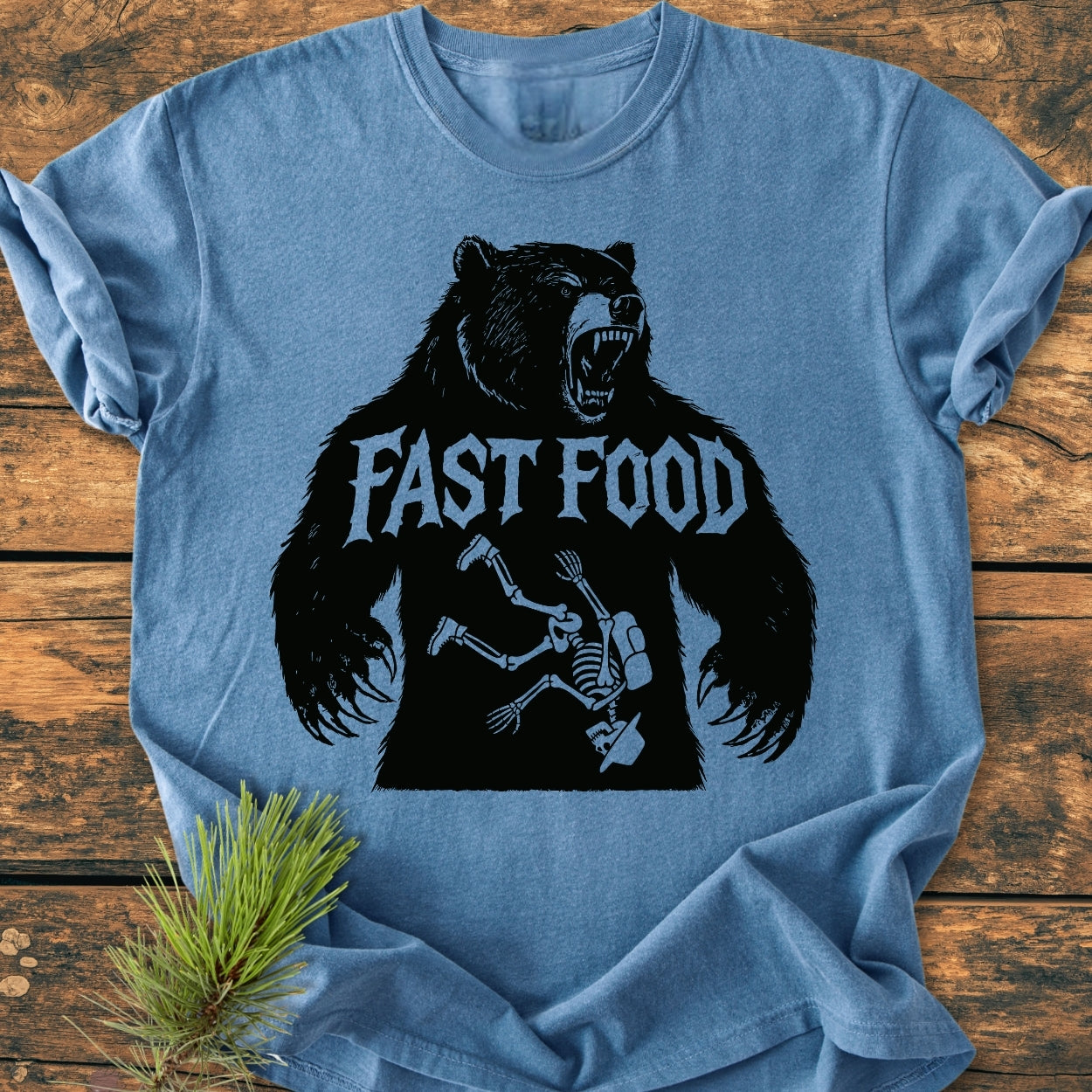 Fast Food - Vintage Wash Tee featuring a roaring bear with FAST FOOD text and skeleton graphic, displayed on a rustic surface with pine sprig, showcasing its relaxed, durable fit and unique design.