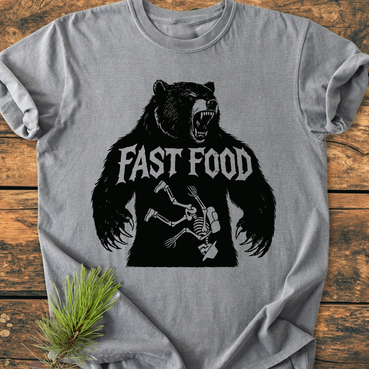 Fast Food - Vintage Wash Tee showcasing a roaring bear silhouette with FAST FOOD text, featuring a cartoon skeleton inside. Laid on wood, it highlights the tee's heather-gray color and cozy, relaxed fit.