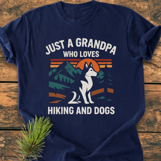 Grandpa Loves Hiking And Dogs - Vintage Wash Tee features a mountain, tree, and sun graphic with a husky, text above and below, laid on wood with pine sprig, showcasing its cozy, relaxed design.