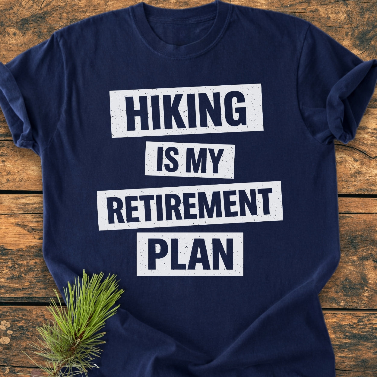 Navy-blue Hiking Is My Retirement Plan - Vintage Wash Tee laid flat with bold white text, on wood. Features a soft, relaxed fit, and includes a pine sprig accent for a natural touch.